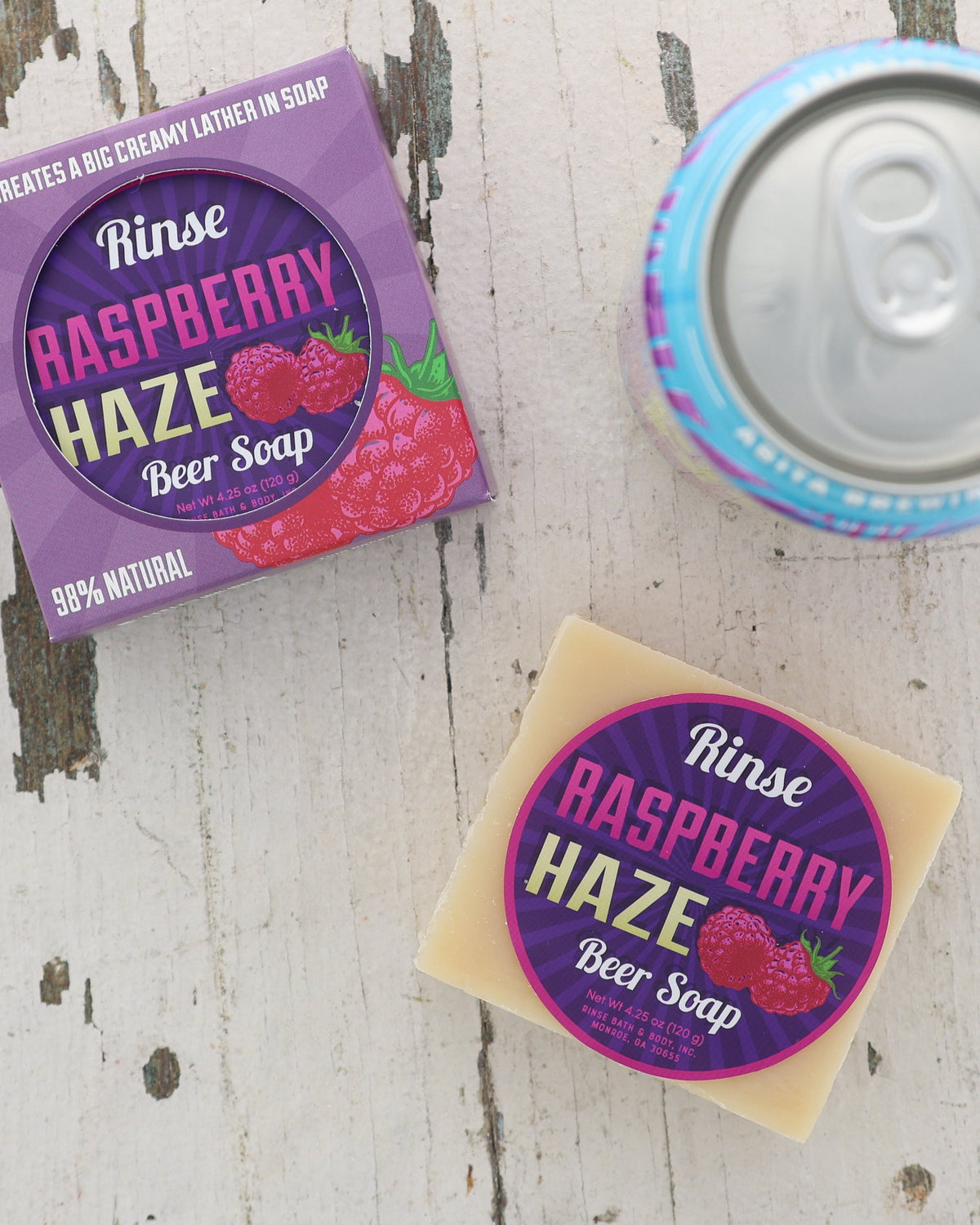 Raspberry Haze beer soap and purple carton rest on weathered white wood — silver can and raspberry art overhead