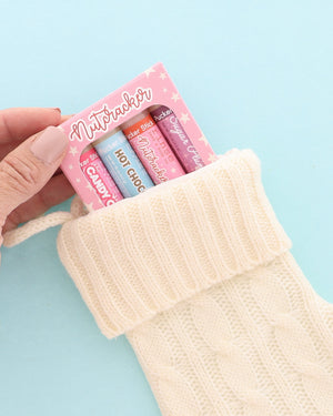 Pink Nutcracker lip balm pack tucked into a cream knit stocking on light blue