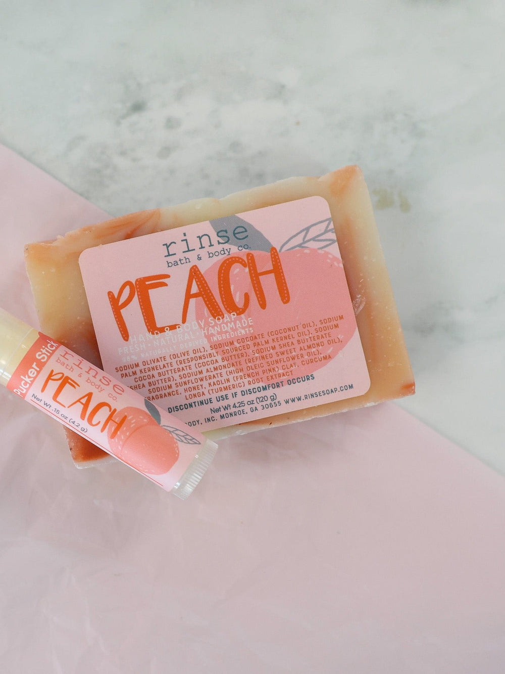 Peach soap and Peach Pucker Stick rest on pink tissue — white marble veins soft underneath