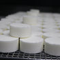 Rows of unwrapped white Peppermint shower bombs cool on a wire rack — chalky discs recede into soft focus