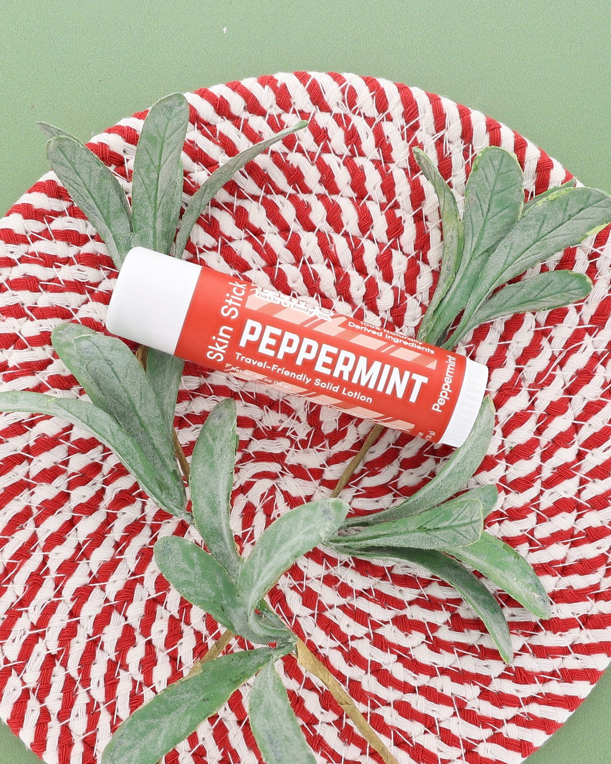 Peppermint Skin Stick on a red and white woven plate with a frosted greenery sprig