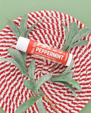 Peppermint Skin Stick on a red and white woven plate with a frosted greenery sprig