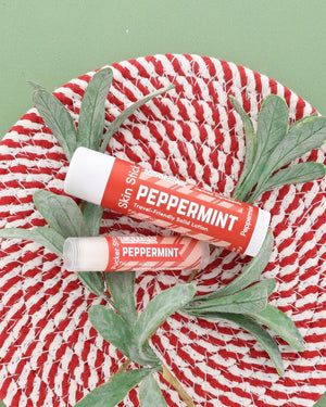 Peppermint Skin Stick and Peppermint Pucker Stick on a red and white woven plate with a frosted greenery sprig