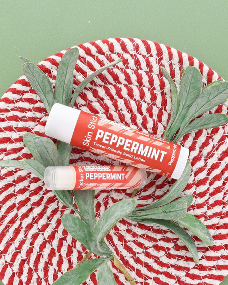Peppermint Skin Stick and Peppermint Pucker Stick on a red and white woven plate with a frosted greenery sprig