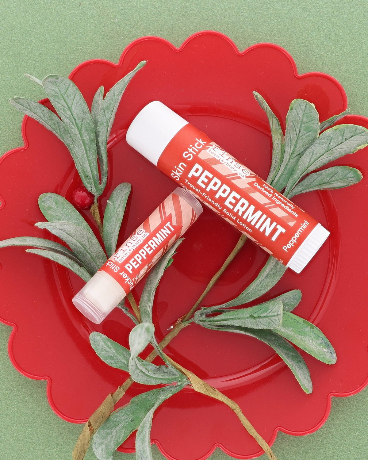 Peppermint Skin Stick and Peppermint Pucker Stick on a red scalloped plate with frosted greenery on sage green