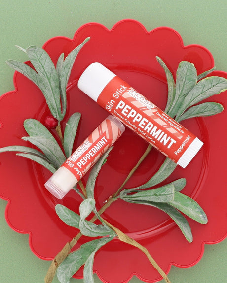 Peppermint Skin Stick and Peppermint Pucker Stick on a red scalloped plate with frosted greenery on sage green