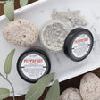 Peppofoot Polish jars styled in a white tray with pumice stones and fresh sage — a pumice-and-peppermint scrub for heels that have earned it. Rinse Bath & Body Co.