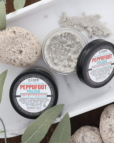 Peppofoot Polish jars styled in a white tray with pumice stones and fresh sage