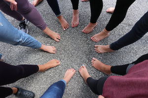 Five pairs of bare feet arranged in a circle on pavement, toes in — the after-the-hike moment Peppofoot spray is made for. Rinse Bath & Body Co.