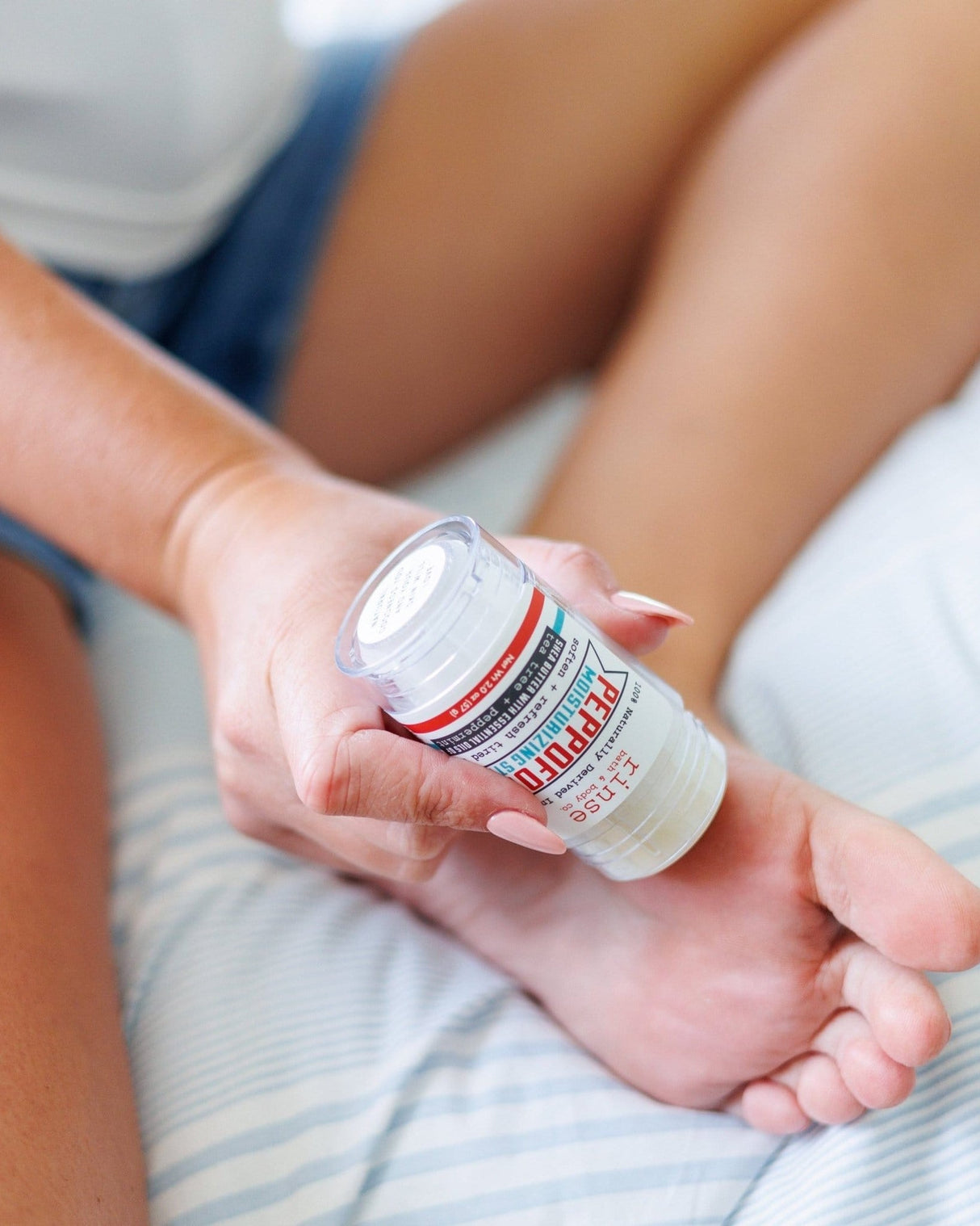 Hands working Peppofoot balm into a bare heel in soft daylight