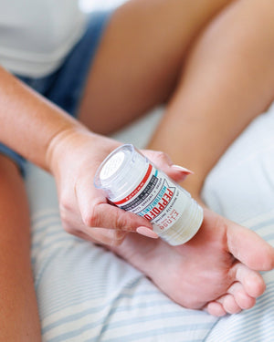 Hands working Peppofoot balm into a bare heel in soft daylight