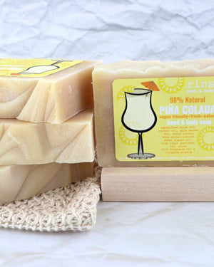 Piña Colada bars stack on a crochet washcloth — upright labeled bar on wood slat in soft white light