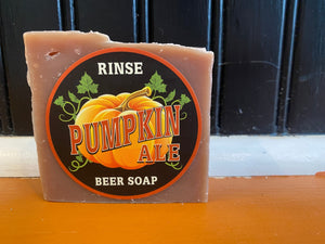 Pumpkin Ale beer soap standing on an orange ledge before dark paneling — pumpkin label and earthy tan bar in autumn light