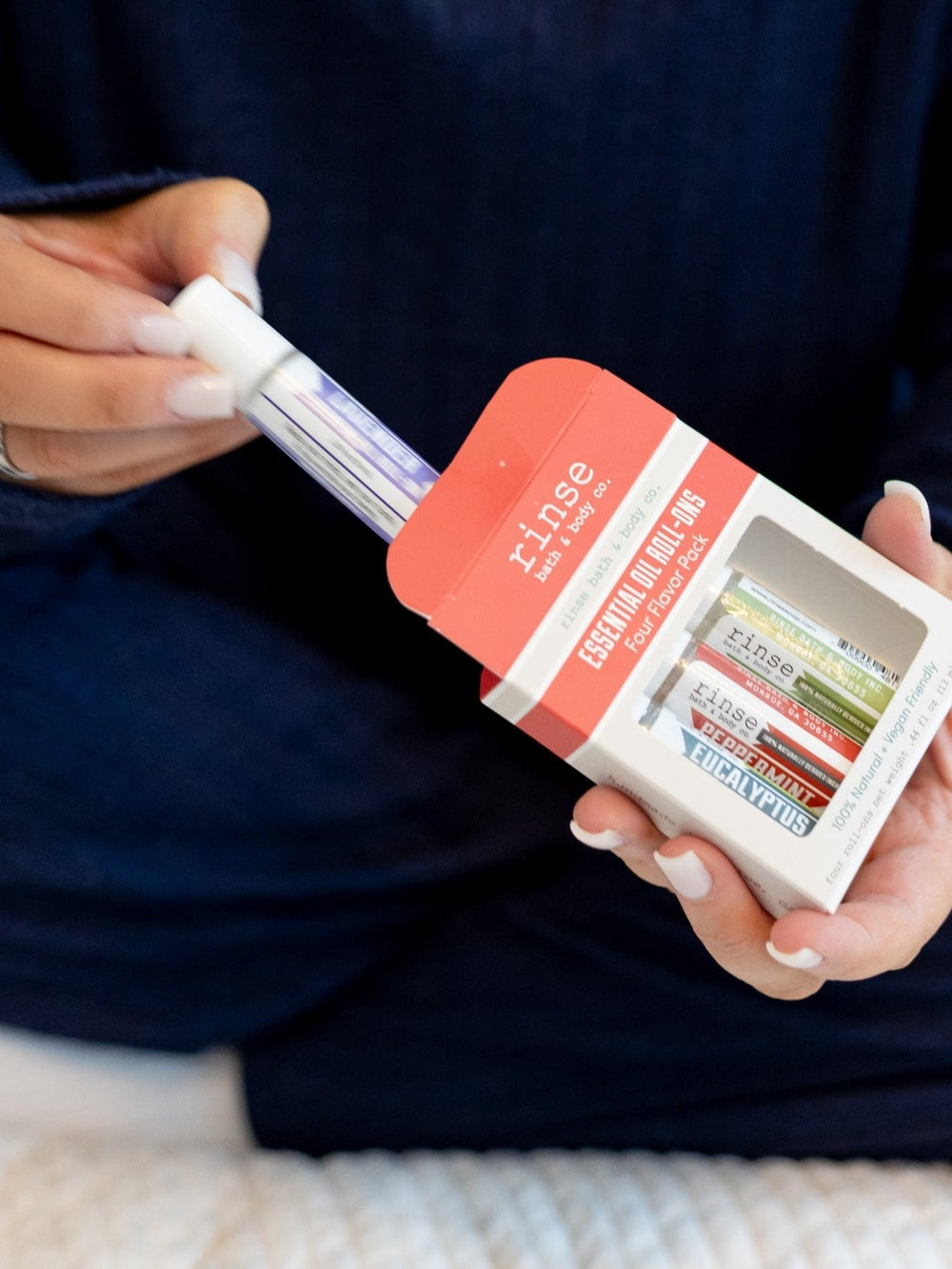 Hands sliding a roll-on from the Four Flavor Pack box — navy sweater sleeves in soft white light