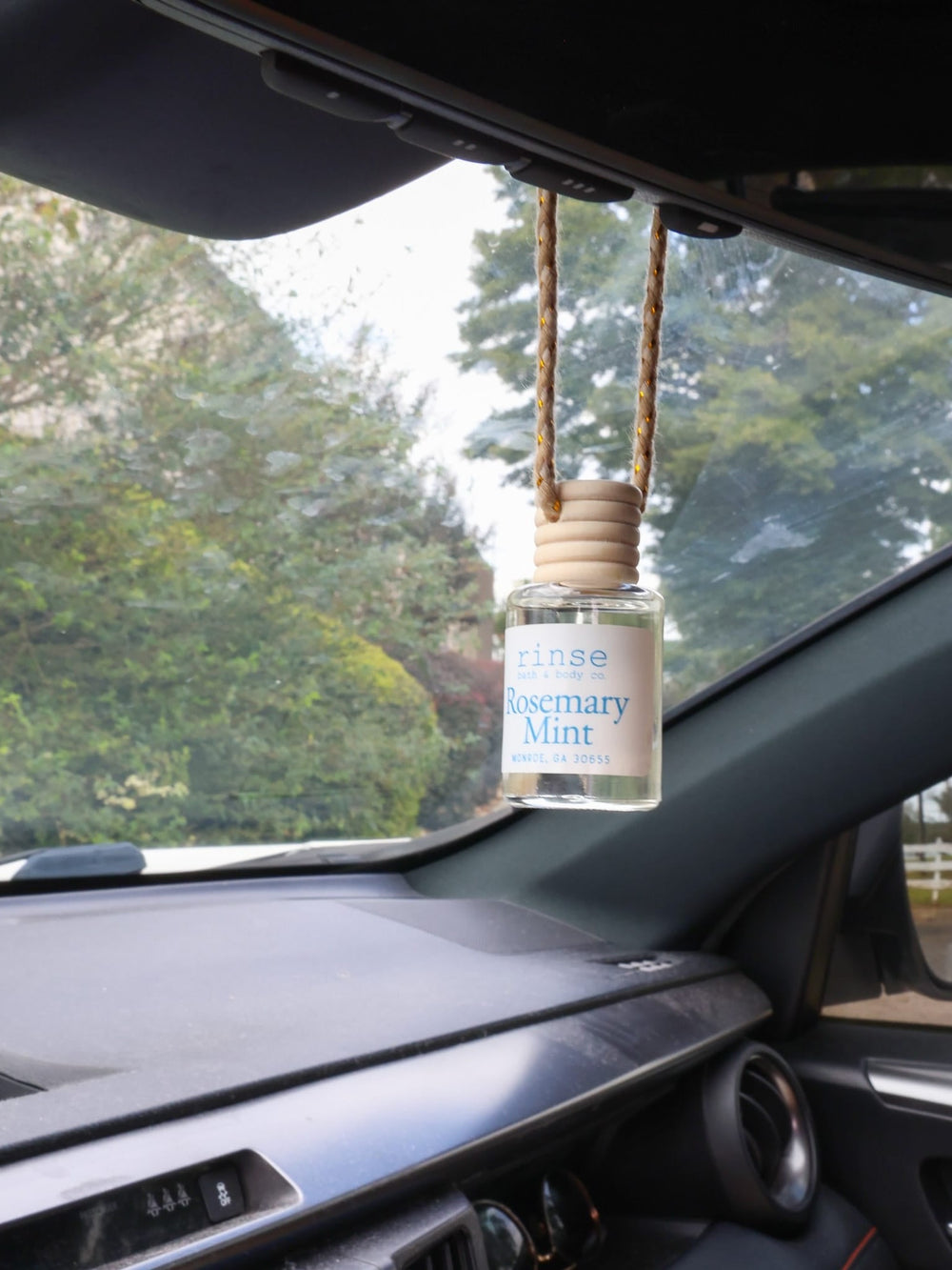Rosemary Mint diffuser hanging from a rearview mirror — green lawn and white fence through the windshield