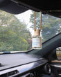 Rosemary Mint diffuser hanging from a rearview mirror — green lawn and white fence through the windshield