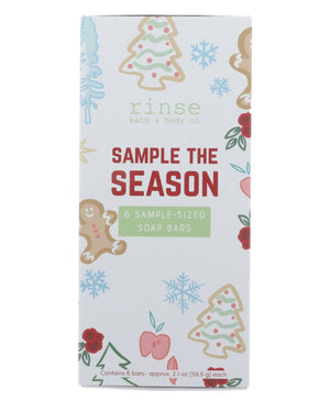 Sample the Season box standing on bright white — gingerbread, tree, snowflake, and berry illustrations with red SAMPLE THE SEASON lettering