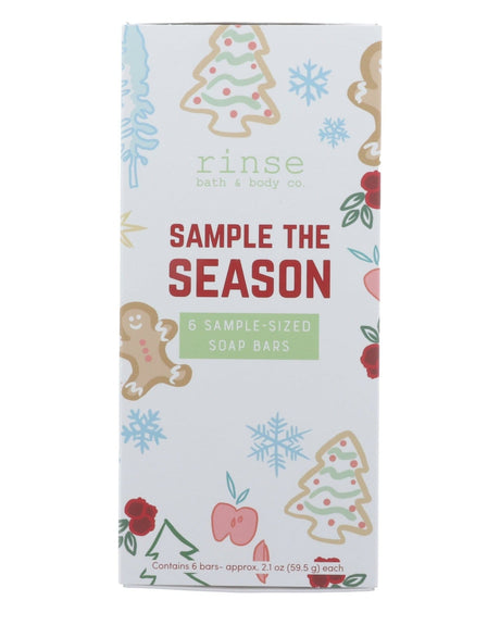 Sample the Season box standing on bright white — gingerbread, tree, snowflake, and berry illustrations with red SAMPLE THE SEASON lettering