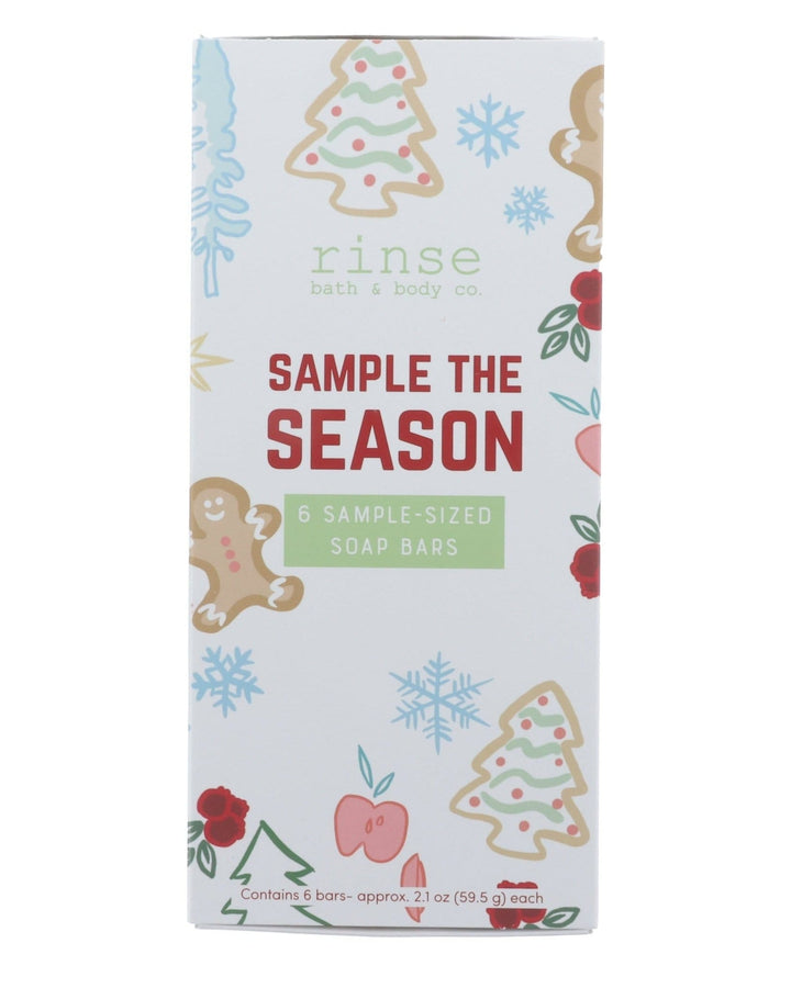 Sample the Season box standing on bright white — gingerbread, tree, snowflake, and berry illustrations with red SAMPLE THE SEASON lettering