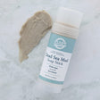 Dead Sea Mud Soap Stick beside a thick taupe smear on cool marble — creamy mineral paste showing fine grit in soft light