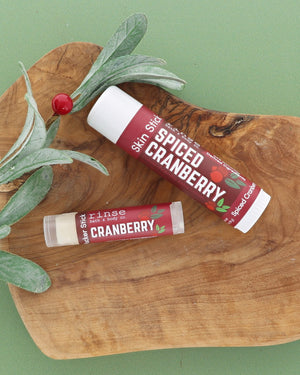 Spiced Cranberry Skin Stick and Cranberry Pucker Stick on an olive wood board with a frosted greenery sprig