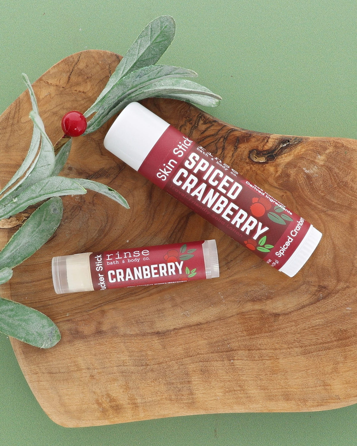 Spiced Cranberry Skin Stick and Cranberry Pucker Stick on an olive wood board with a frosted greenery sprig