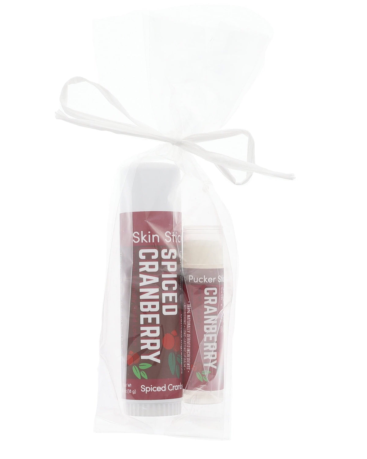 Spiced Cranberry Skin Stick and Pucker Stick lifestyle on bright white — maroon labels in soft studio light