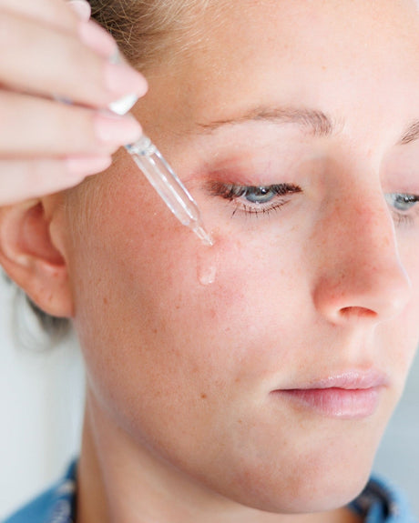 A woman holding the glass dropper to her cheek, releasing Squalane Face Oil onto the skin. Rinse Bath & Body Co.