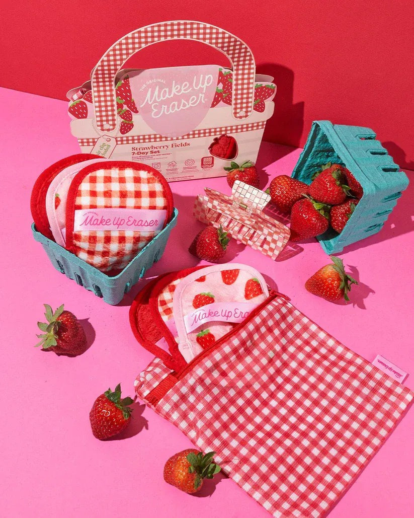 Strawberry Fields MakeUp Eraser picnic flat lay — carton, seven cloths, gingham laundry bag, and hair clip with fresh strawberries