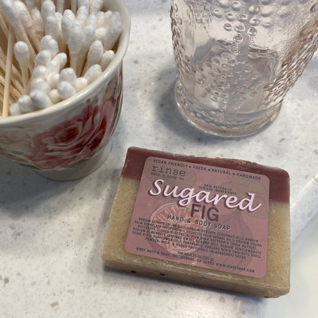 Wrapped Sugared Fig soap on speckled marble beside a rose cup of cotton swabs — bright bathroom counter light