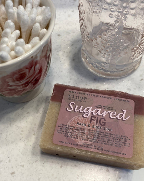 Wrapped Sugared Fig soap on speckled marble beside a rose cup — bathroom counter lifestyle flat lay