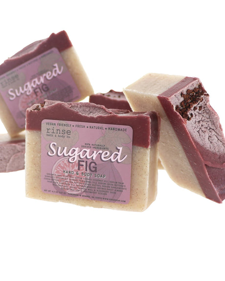 Sugared Fig soap stylized flat lay — cream bars with deep plum seed-dusted tops stacked on bright white