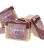 Sugared Fig soap stylized flat lay — cream bars with deep plum seed-dusted tops stacked on bright white