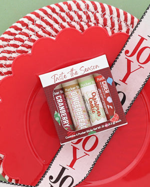 Taste the Season lip balm pack with Christmas Cookie, Cranberry and Gingerbread Pucker Sticks on a red woven plate with a JOY ribbon