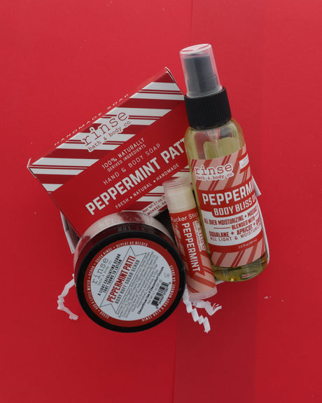 A gift set of five 'Since Nature' peppermint products arranged on a bright red background, including a hand and body soap bar, a peppermint body spray, a peppermint lip balm, a peppermint soap bar, and a peppermint hand and body soap box.