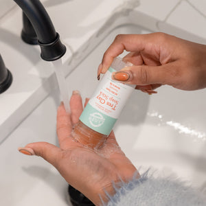 Hands rubbing Tres Clay Soap Stick into a palm under a black faucet — terracotta soap and white lather at a modern sink