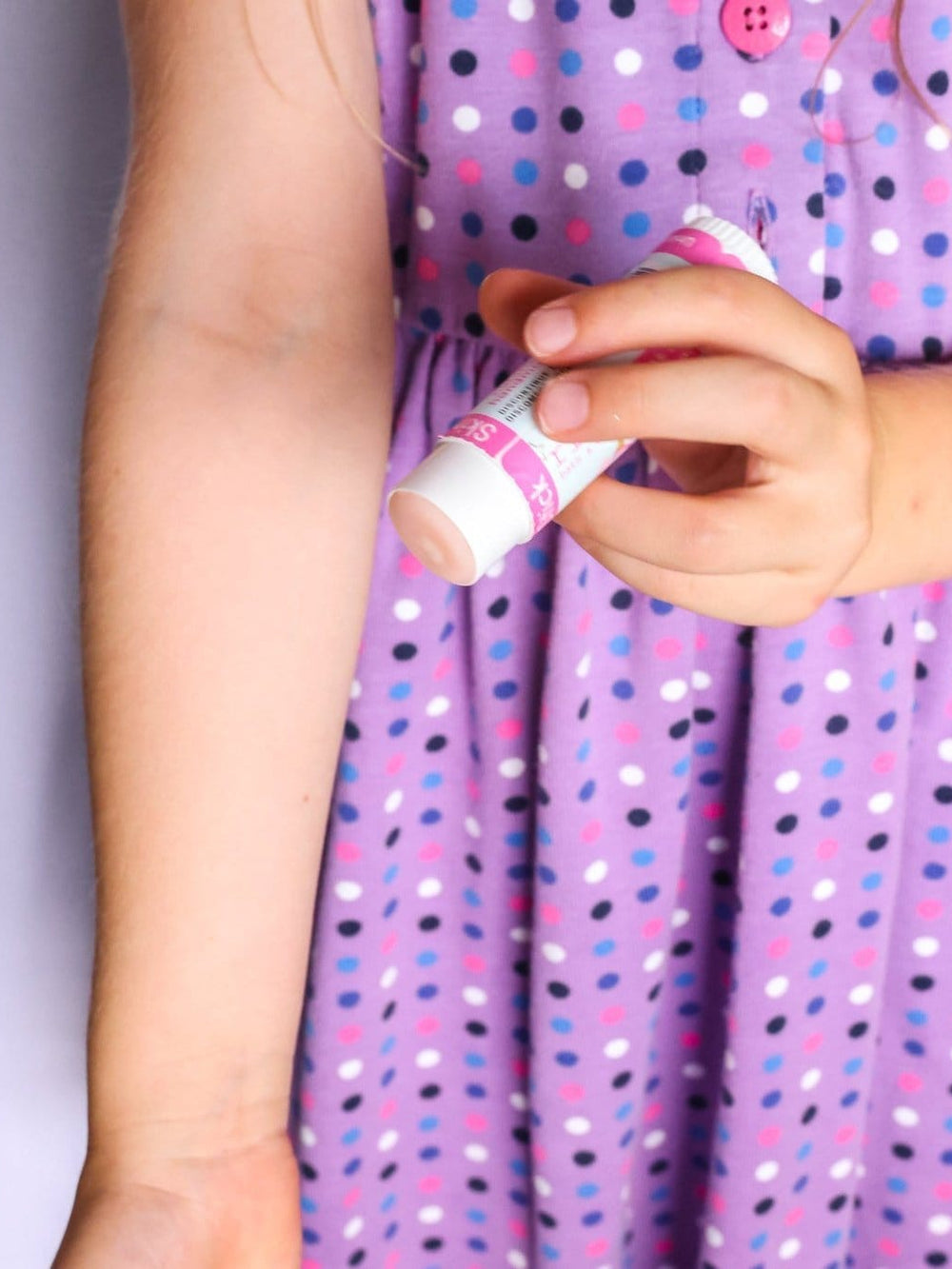 Child's hand gliding Unicorn Magic Skin Stick over a forearm — purple polka-dot dress in bright room light