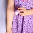 Child's hand gliding Unicorn Magic Skin Stick over a forearm — purple polka-dot dress in bright room light