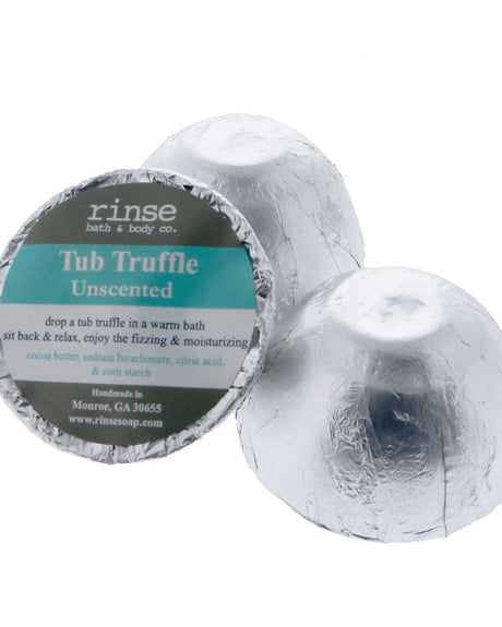 A silver foil-wrapped Unscented Tub Truffle beside a second one cut open to show the cocoa butter dome, on white — no scent, all cocoa butter. Rinse Bath & Body Co.