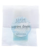 Warm Linen soap slice rests in crinkled translucent paper under a soft blue circular label on bright white.