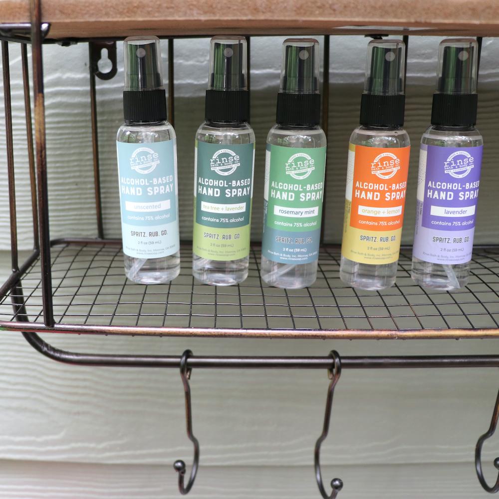 Five colorful hand sprays line a rustic wire basket — sunlit exterior siding behind