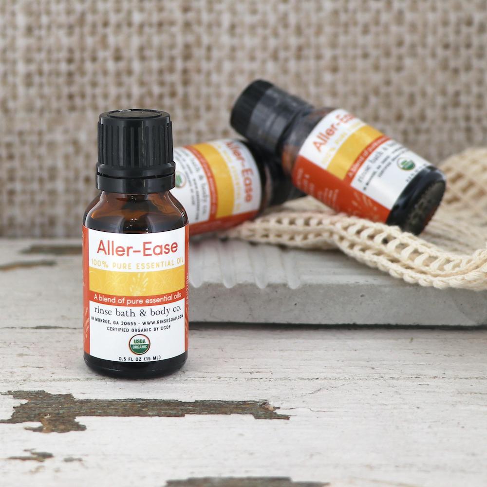 Aller-Ease bottles on weathered white wood with a knitted cloth and stone slab — amber glass and orange labels in bright natural light