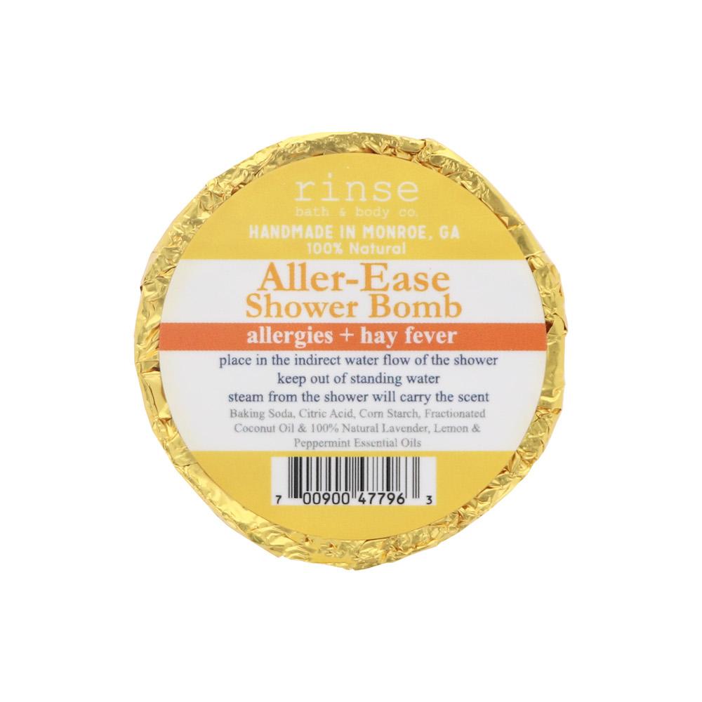 Gold-foil Aller-Ease Shower Bomb centered on bright white — yellow-orange circular label in studio light