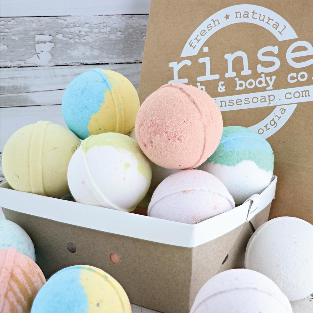 Assorted pastel bath bombs nest in a white berry basket — Rinse bag and whitewashed wood behind