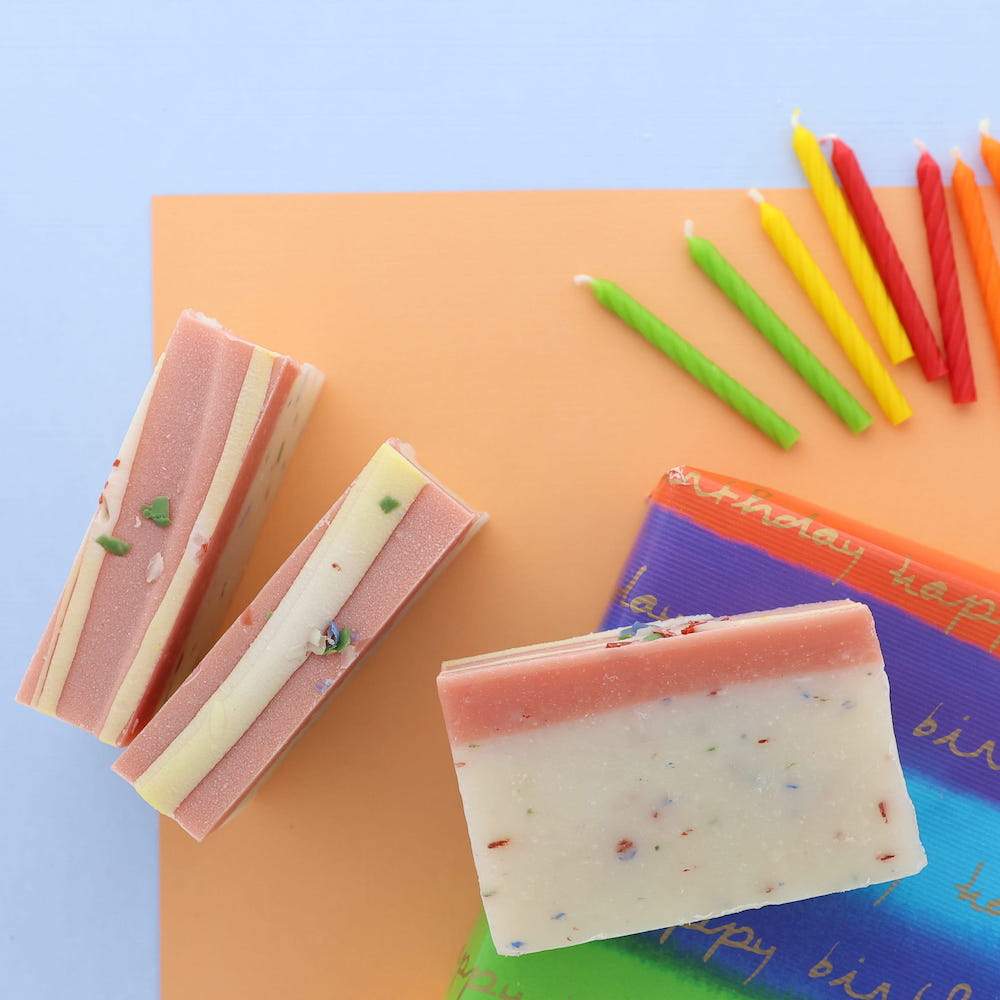 Birthday Cake soap slices scatter with unlit candles — tissue paper on blue and orange flat-lay