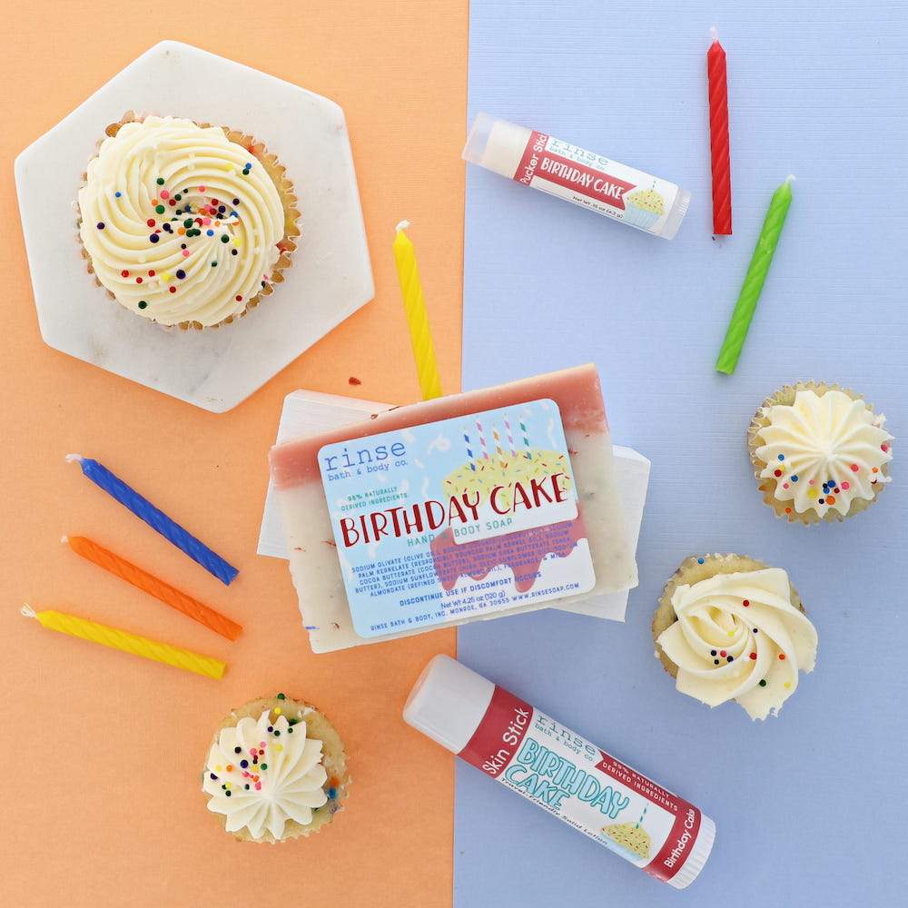 Birthday Cake bar soap, solid lotion stick and lip balm styled with frosted cupcakes and lit candles — the gift that reads as a party. Rinse Bath & Body Co.