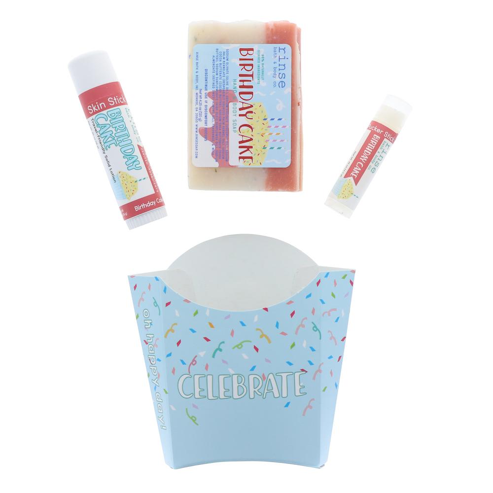 The Birthday Cake set laid out flat — bar soap, solid lotion skin stick and lip balm above the pale blue CELEBRATE carton. Rinse Bath & Body Co.