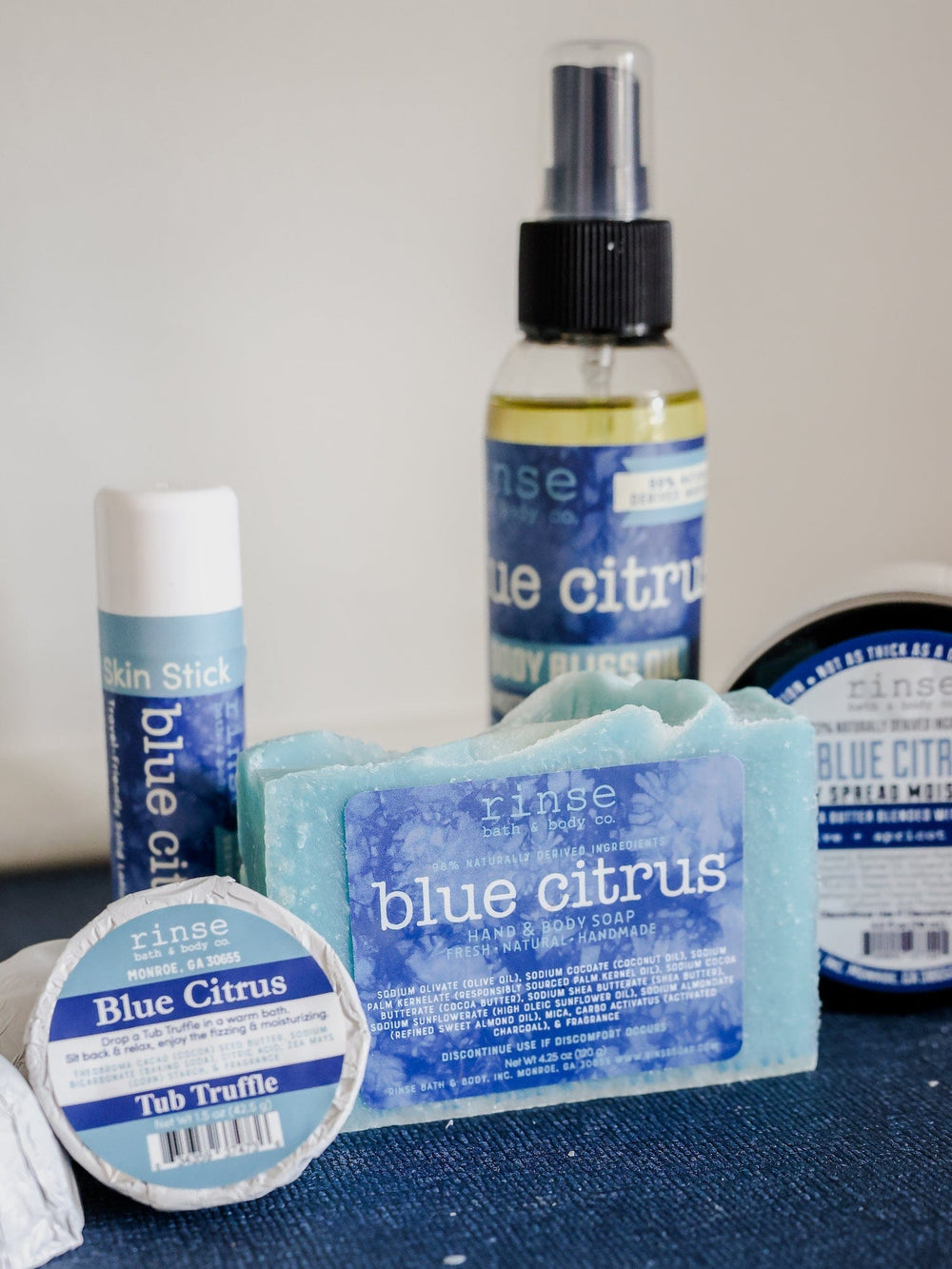 Blue Citrus soap with Tub Truffle Skin Stick oil and Body Spread — dark blue fabric studio display