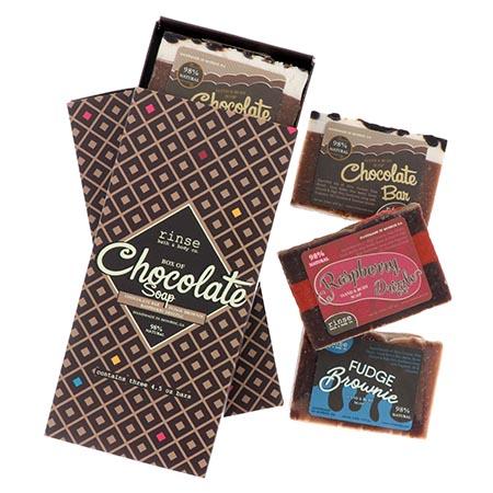Box of Chocolate Soap sleeve with three dessert bars stacked on white — cream-topped cocoa, raspberry stripe, and fudge brownie