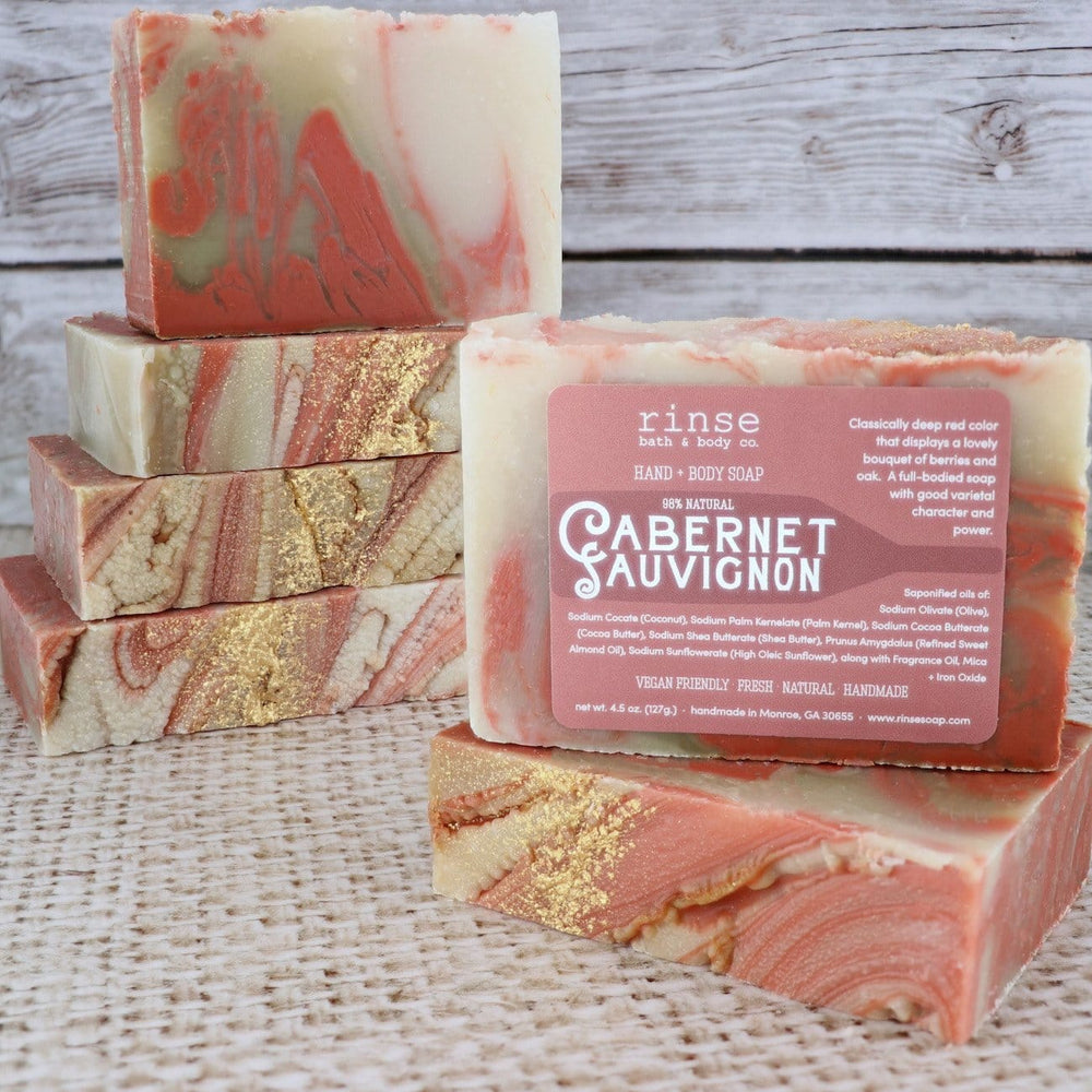 Cabernet Sauvignon soap bars rest on textured burlap — weathered wood planks behind in warm light